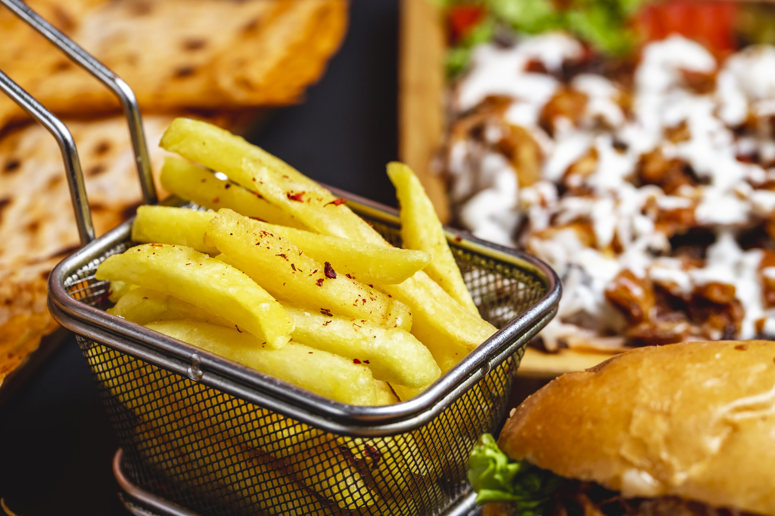side view french fries in stainless steel mini basket with salt and burger on the table